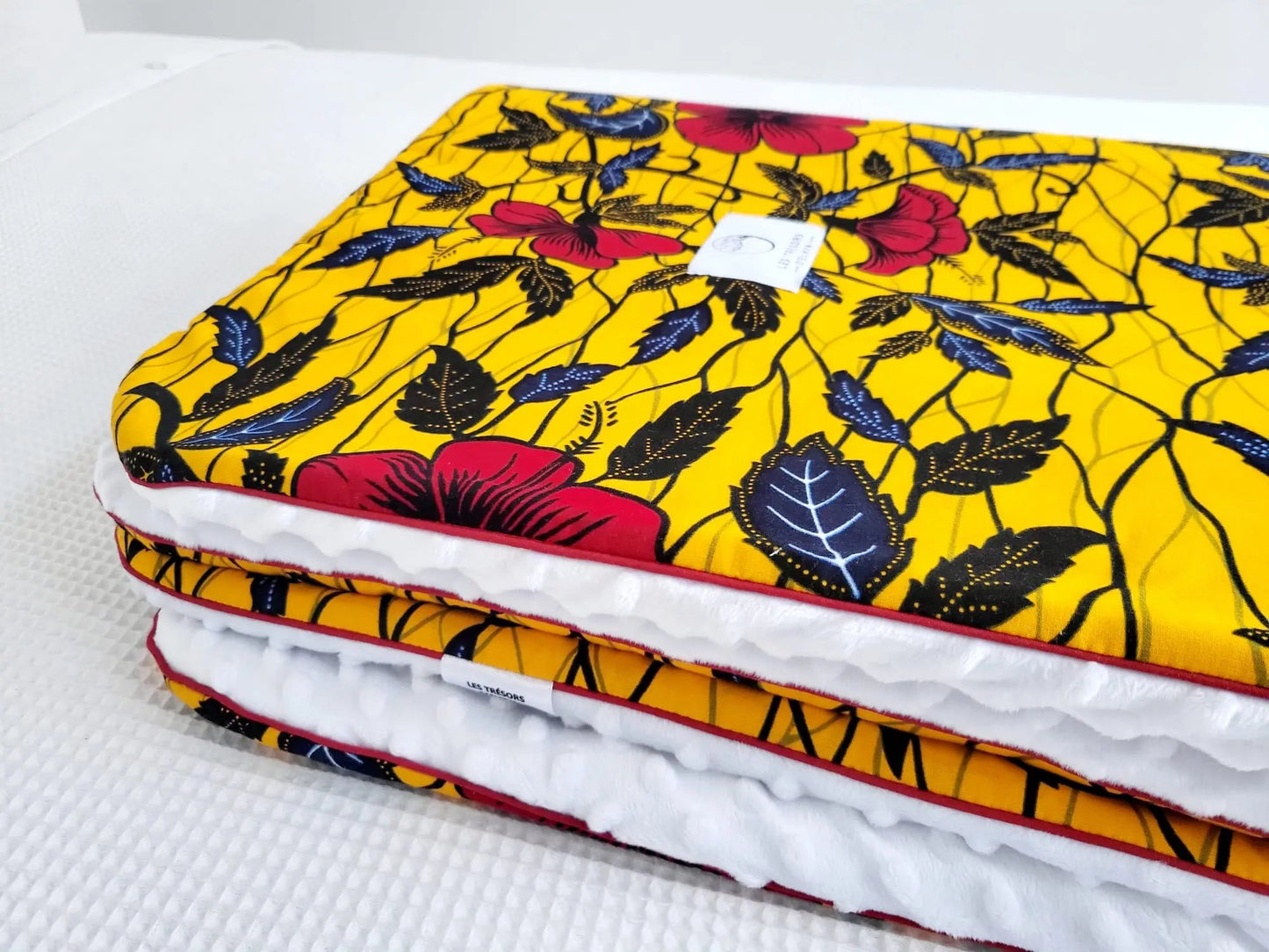 Zoom sur le carré de la couverture AYANA– tissu wax africain aux motifs floraux rouges et noirs, doublure minky ultra douce et finitions passepoils élégantes. Création artisanale Les Trésors d’Elikya pour envelopper bébé de douceur.