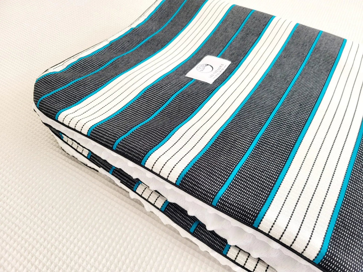 Zoom sur le carré de la couverture koba – tissu wax africain aux tissu Wax aux lignes turquoise délicatement tracées, dans une danse équilibrée de noir profond et de blanc éclatant, doublure minky ultra douce et finitions passepoils élégantes. Création artisanale Les Trésors d’Elikya pour envelopper bébé de douceur.