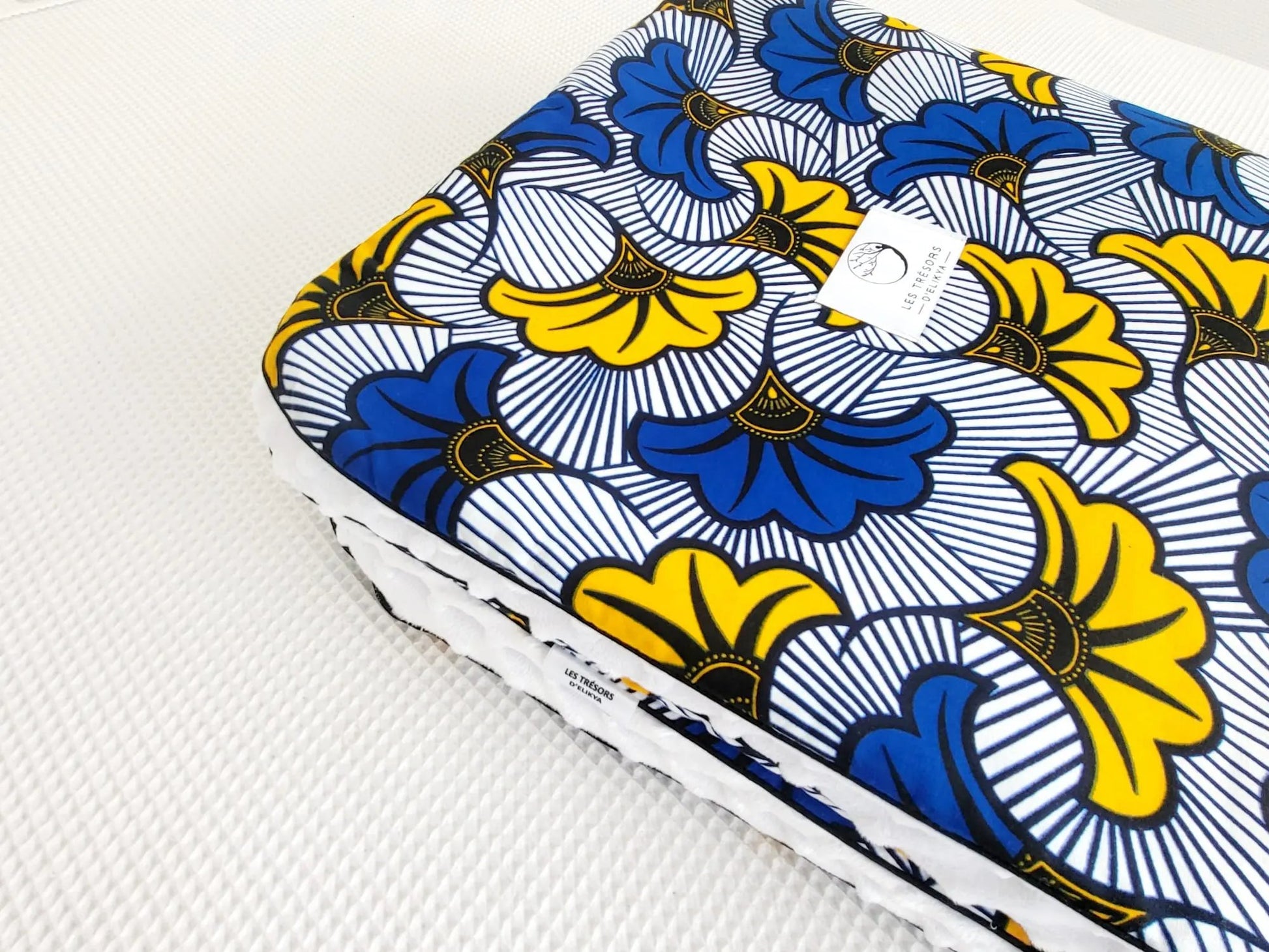 Zoom sur le carré de la couverture MIRELYS – tissu wax fleurs de mariage jaunes et bleues sur fond blanc, doublure minky ultra douce et finitions passepoils élégantes. Création artisanale Les Trésors d’Elikya pour envelopper bébé de douceur.