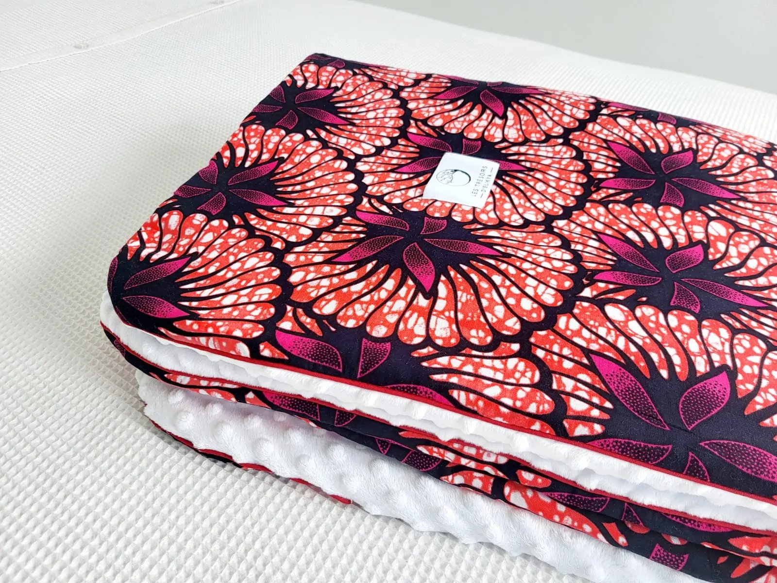 Zoom sur le carré de la couverture ROSÉLIA – tissu wax africain aux motifs floraux roses et noirs, doublure minky ultra douce et finitions passepoilées élégantes. Création artisanale Les Trésors d’Elikya pour envelopper bébé de douceur.