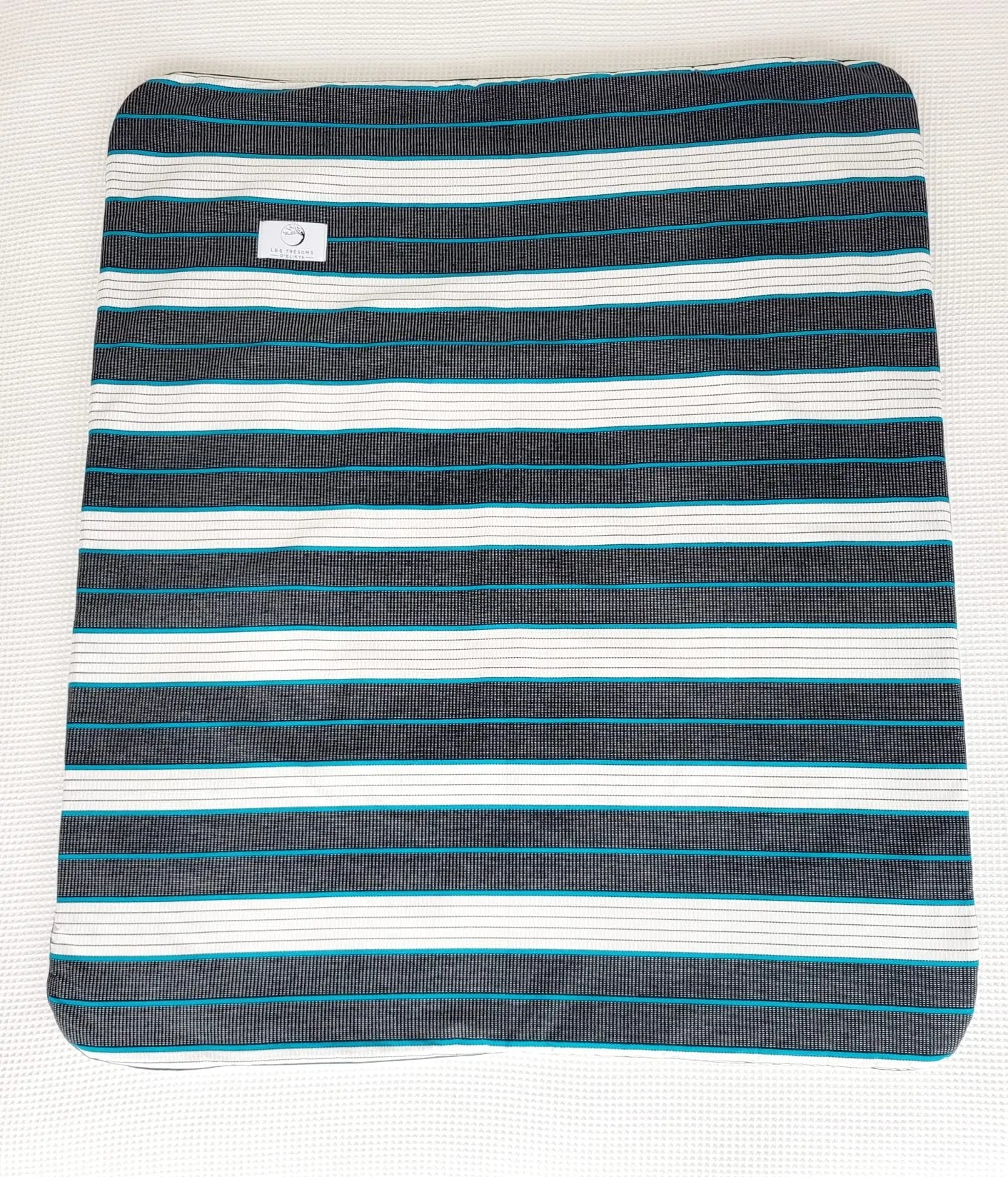 Vue complète de la couverture koba– face en tissu wax africain aux lignes turquoise délicatement tracées, dans une danse équilibrée de noir profond et de blanc éclatant. Confection artisanale Les Trésors d’Elikya. Couverture bébé douce, moelleuse et raffinée, idéale comme cadeau de naissance.
