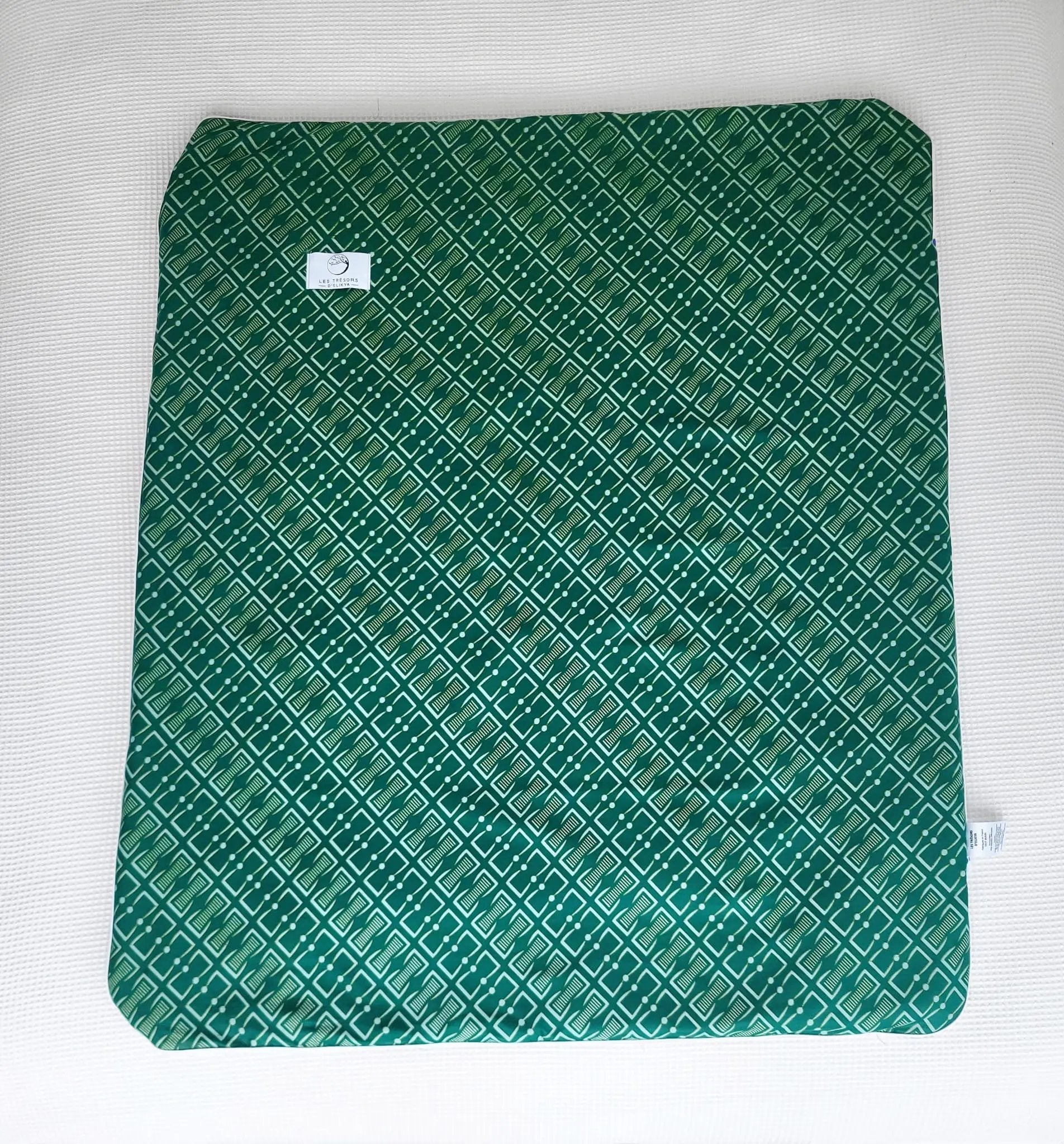 Vue complète de la couverture NAIORIA– face en tissu wax africain aavec un motif graphique vert profond orné de formes géométriques ivoire et de pois réguliers, confection artisanale Les Trésors d’Elikya. Couverture bébé douce, moelleuse et raffinée, idéale comme cadeau de naissance.