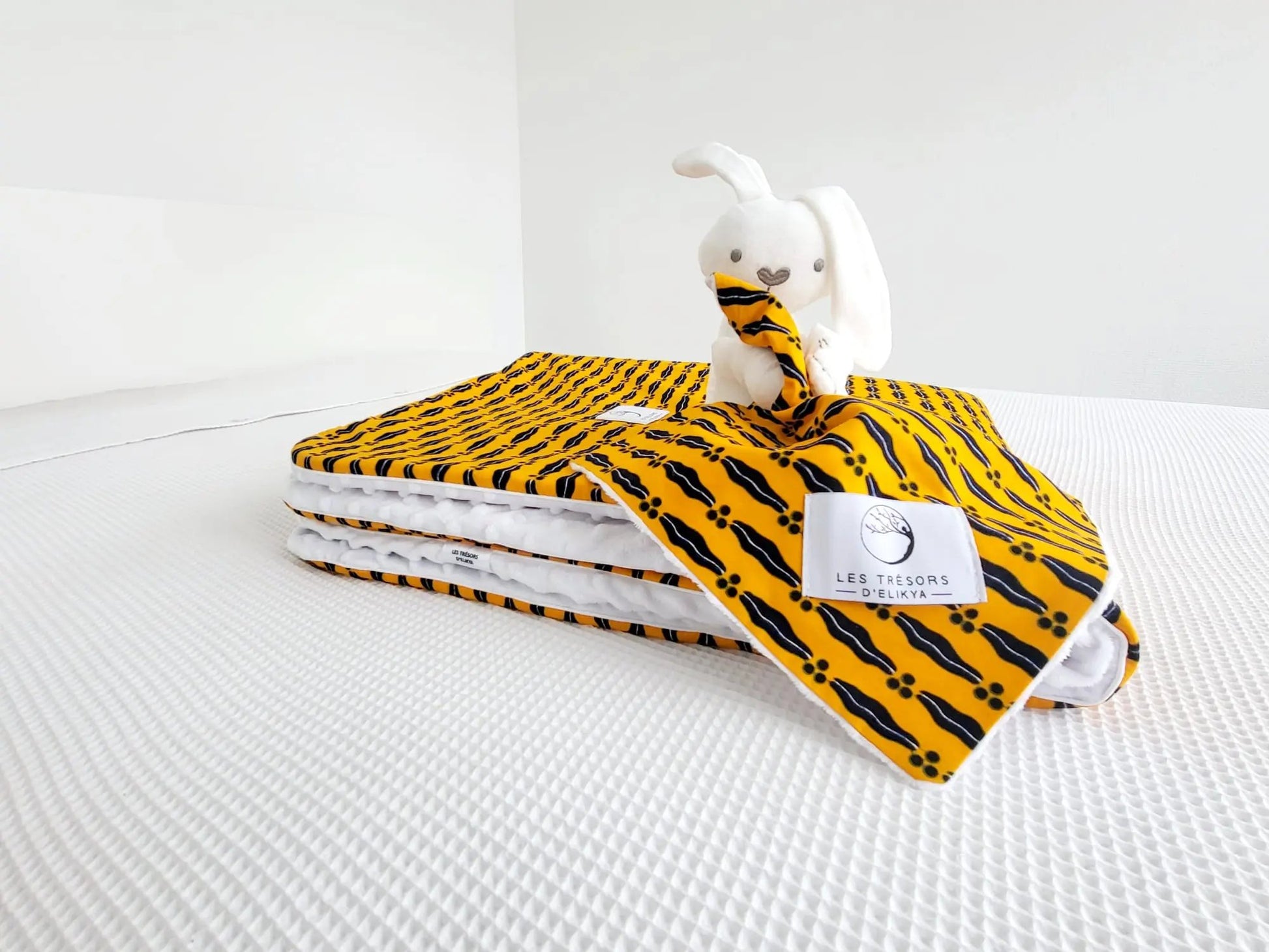 Zoom sur la mini couverture du doudou Bunny Wax JASIRI et l’étiquette Les Trésors d’Elikya – peluche bébé avec sa mini couverture faite main en tissu wax africain Mon mari est capage. Détail de confection artisanale et idée de cadeau de naissance unique.