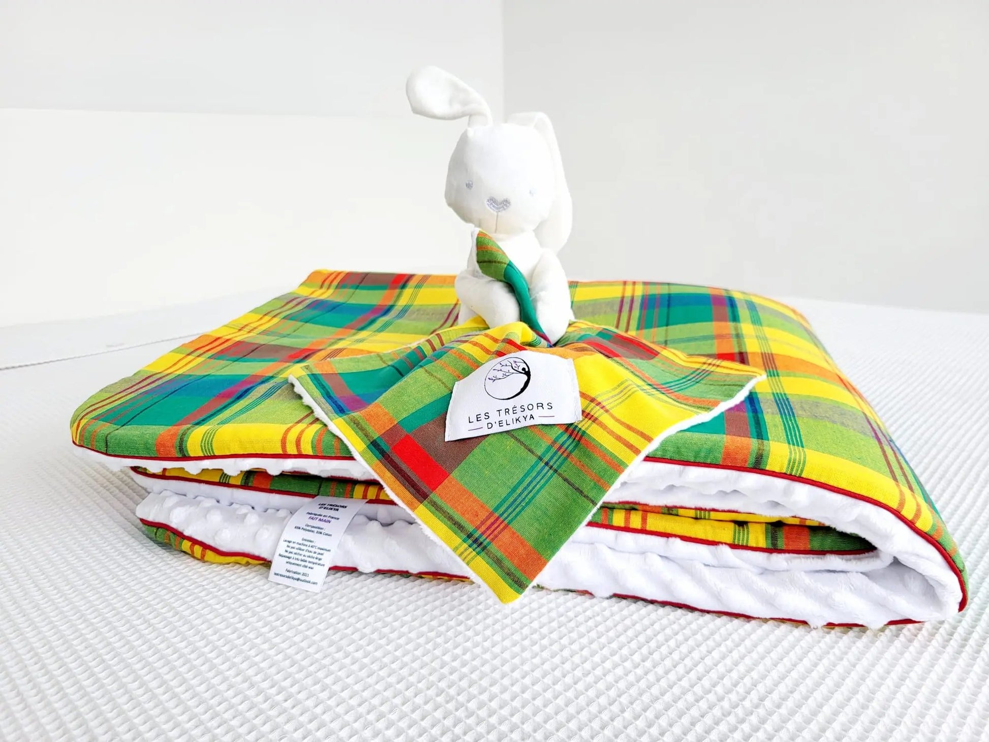 Zoom sur la mini couverture du doudou Bunny Madras MADELYOS et l’étiquette Les Trésors d’Elikya – peluche bébé avec sa mini couverture faite main en tissu madras antillais vert, rehaussé de lignes jaunes et rouges. Détail de confection artisanale et idée de cadeau de naissance unique.