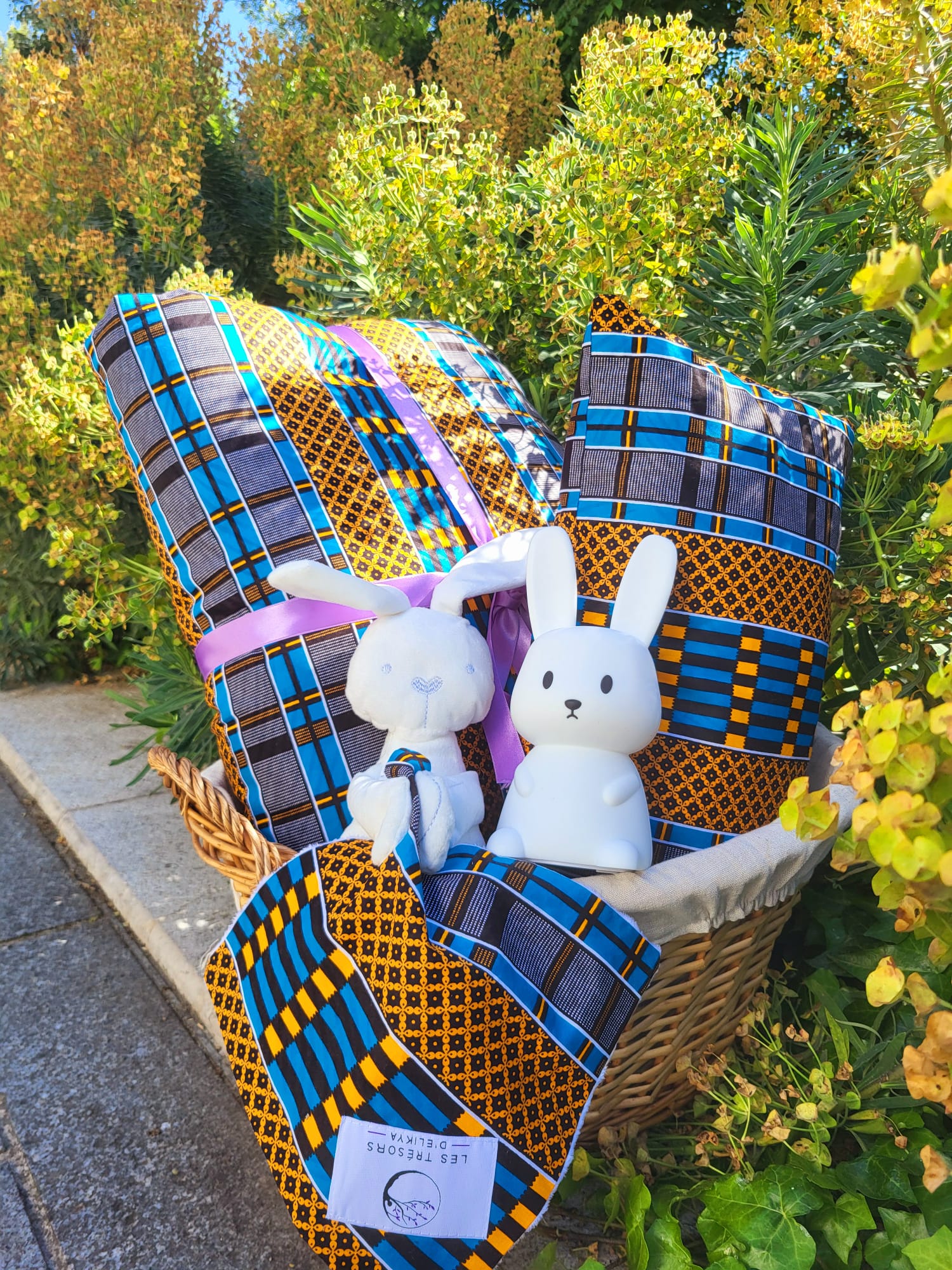 Coffret naissance Écrin Suprême AMANI – ensemble complet avec couverture, coussin, doudou lapin et accessoires en tissu Wax bleu et jaune, dans un panier fait main – Les Trésors d’Elikya