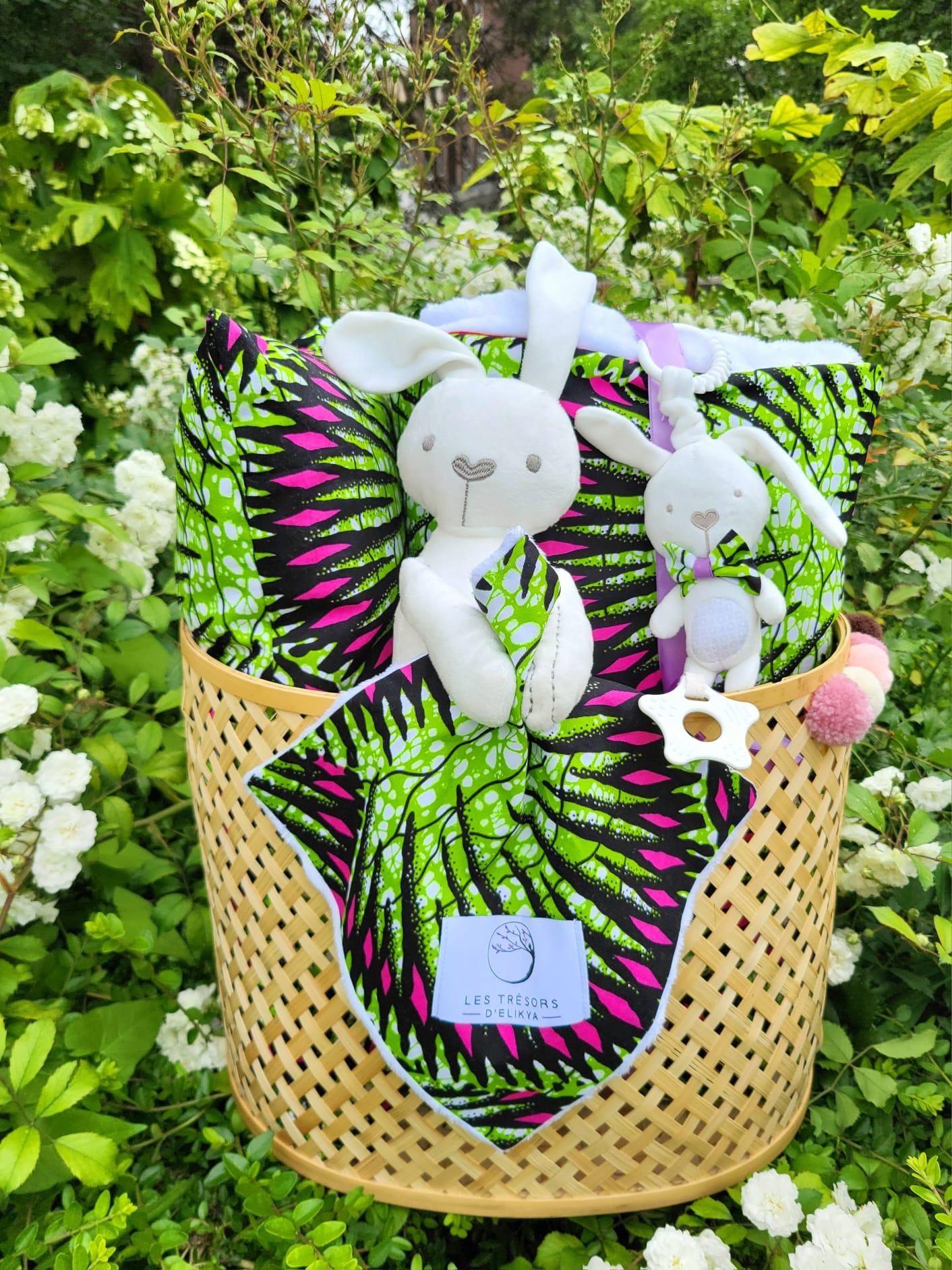 Coffret naissance Écrin Douceur NÉOLYS – doudou lapin, couverture et accessoires assortis en tissu Wax vert et rose, présentés dans un panier artisanal – Les Trésors d’Elikya